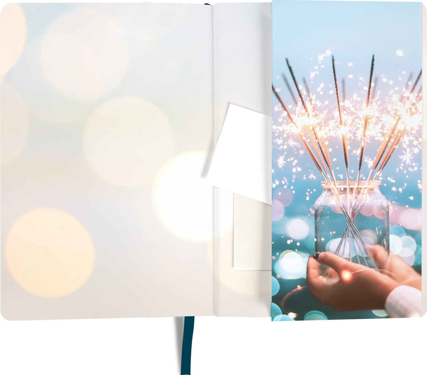 Gezeigt wird eine Innen- oder Zusatzansicht von „myNOTES Notizbuch A6: The magic is in you“. Die Ansicht zeigt eine sanfte, hellblau-türkise Hintergrundfarbe mit einem Glanz von Lichtpunkten. Auf der rechten Seite ist eine Hand zu sehen, die eine Glaskaraffe mit brennenden Wunderkerzen hält. Die gesamte Illustration strahlt eine festliche Stimmung aus. Die typografischen Elemente sind modern und klar gestaltet, was die positive Botschaft des Notizbuchs unterstreicht.