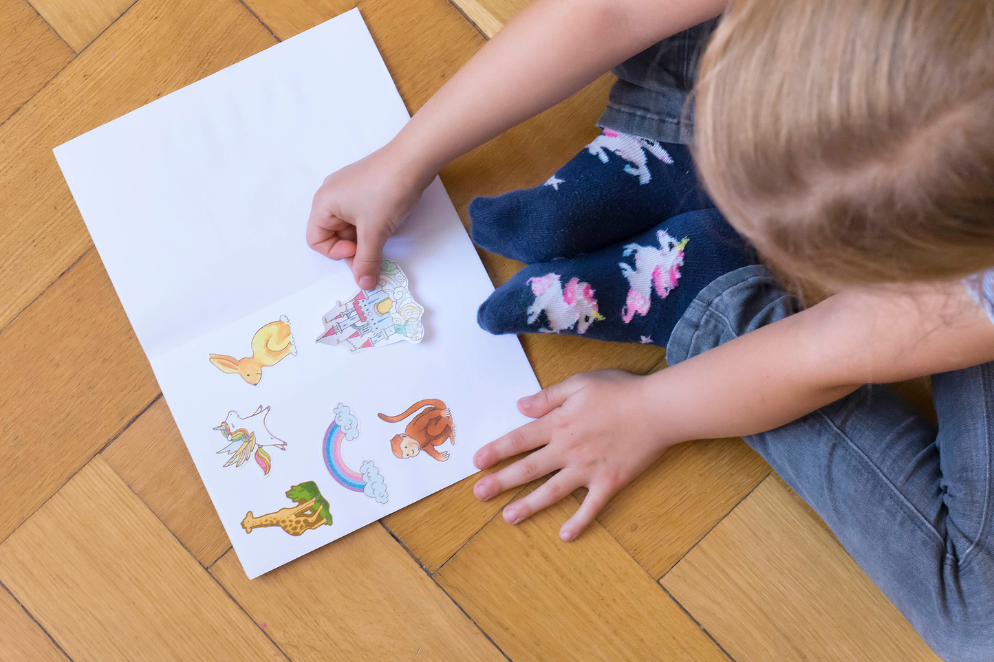 Gezeigt wird eine Innen- oder Zusatzansicht von „Mein Stickeralbum – Weltall“. Auf einer weißen Seite sind bunte, kindgerechte Sticker abgebildet, darunter ein Schloss, ein Regenbogen, ein Hase, ein Regenbogen, ein Affe und weitere fantasievolle Motive. Die Farbpalette ist lebhaft und bunt, mit dominierenden Pastelltönen. Die Typografie ist spielerisch und leicht lesbar, was zur freundlichen und einladenden Gestaltung des Albums beiträgt.