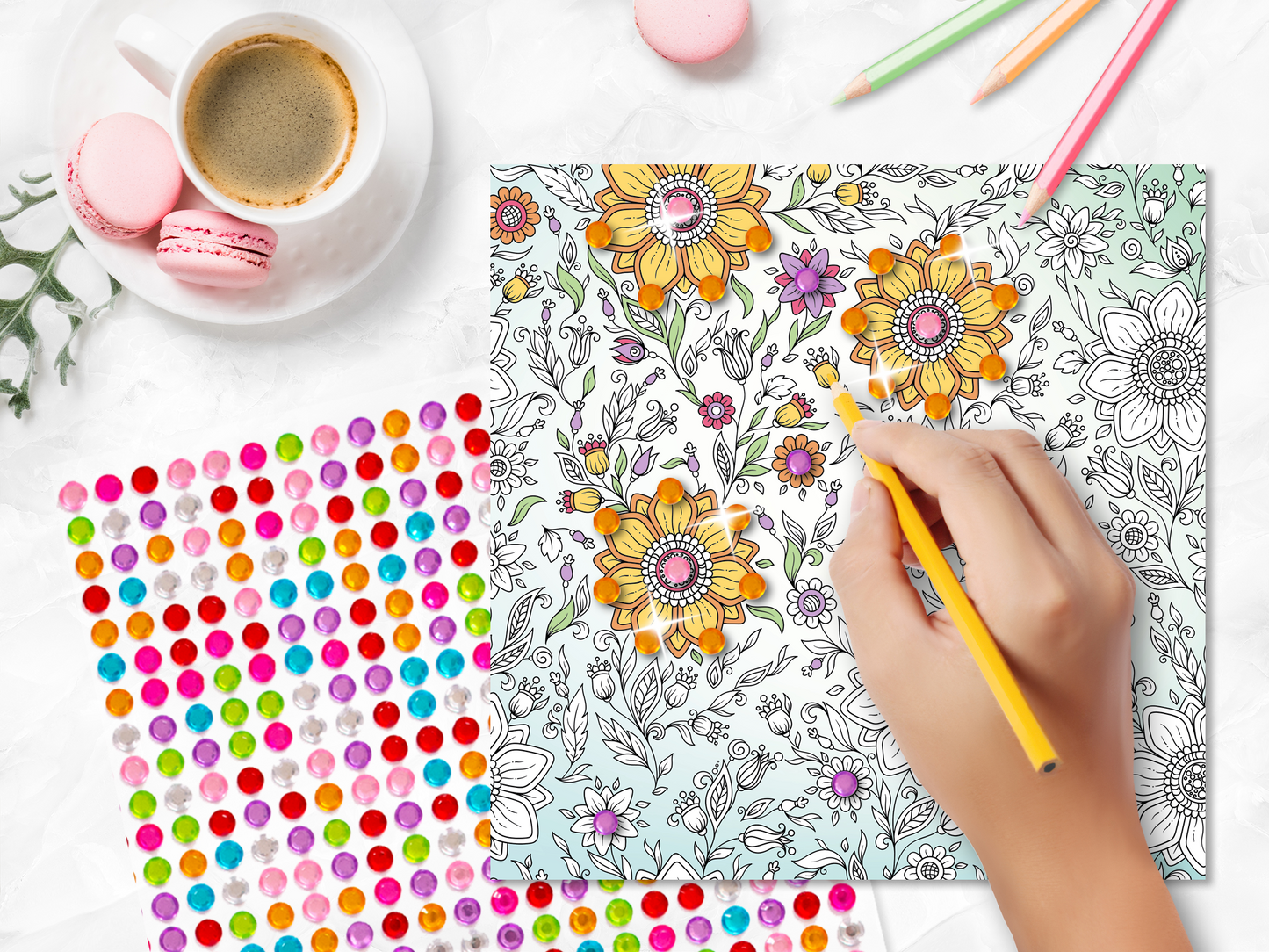 Gezeigt wird eine Innen- oder Zusatzansicht von „Diamond Blütenzauber“. Auf der Abbildung sind bunte, handgezeichnete Blumenmuster in Gelb, Lila und Rosa zu sehen, die auf einem hellblauen Hintergrund angeordnet sind. Ein Bleistift ist sichtbar, während er gerade eine Blüte ausmalt. Rechts daneben liegt ein Bogen mit bunten, glitzernden Punkten in verschiedenen Farben. Im Hintergrund befindet sich eine Tasse Kaffee und einige Macarons, die für eine entspannte Ausmalatmosphäre sorgen.