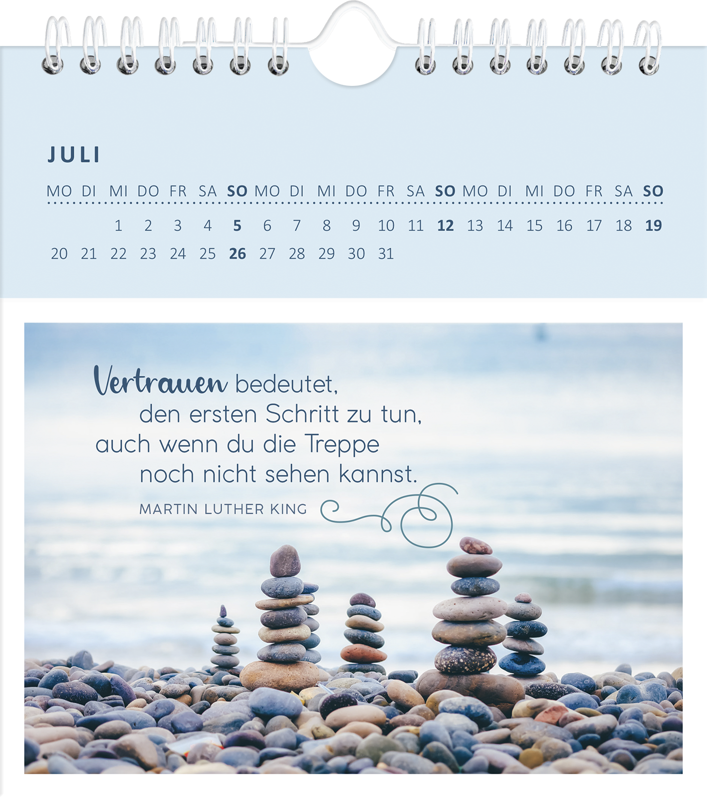 Gezeigt wird eine Innen- oder Zusatzansicht von „Wandkalender Gelassenheit für dich 2026“. Die Ansicht zeigt den Monat Juli, gekennzeichnet durch eine helle, sanfte Farbpalette in Blau- und Grautönen. Die oberste Zeile enthält den Monatsnamen, während der Kalender in einem klaren und leserlichen Typografie-Design die Wochentage anzeigt. Im Vordergrund steht ein inspirierendes Zitat von Martin Luther King, umgeben von einer Fotografie von sorgfältig gestapelten Steinen am Wasser, was...