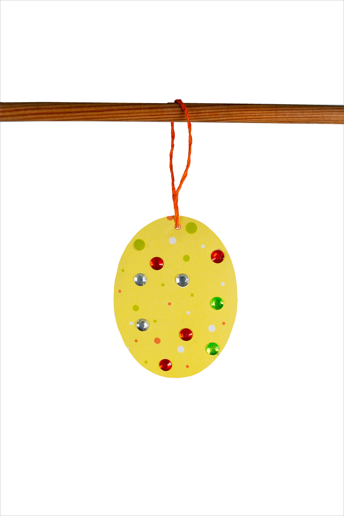 Gezeigt wird eine Innen- oder Zusatzansicht von „Diamant-Oster-Anhänger“. Der Anhänger hat eine ovale Form in leuchtendem Gelb, geschmückt mit bunten Punkten in Grün, Rot und Silber. Er hängt an einem orangen Faden und ist auf einem Holzstab angebracht. Die Farben wirken fröhlich und einladend, was ihn zu einem ideaal Osterschmuckstück macht. Die Typografie ist nicht sichtbar, da es sich um einen dekorativen Anhänger handelt.
