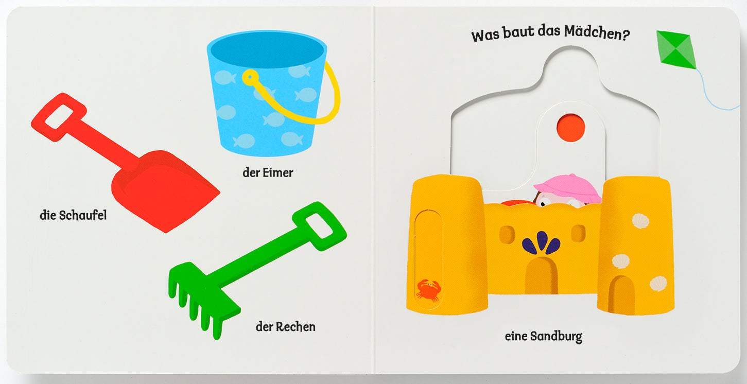 Gezeigt wird eine Innen- oder Zusatzansicht von „Mein erstes Buch vom Meer“. Auf der linken Seite sind ein blauer Eimer, eine rote Schaufel und ein grüner Rechen abgebildet. Die Werkzeuge sind farbenfroh gestaltet und klar erkennbar. Auf der rechten Seite steht die Frage „Was baut das Mädchen?“ neben einer Darstellung einer fröhlichen Sandburg mit rosa Deko-Elementen. Die Schrift ist kindgerecht und gut lesbar, mit einer einladenden Typografie.
