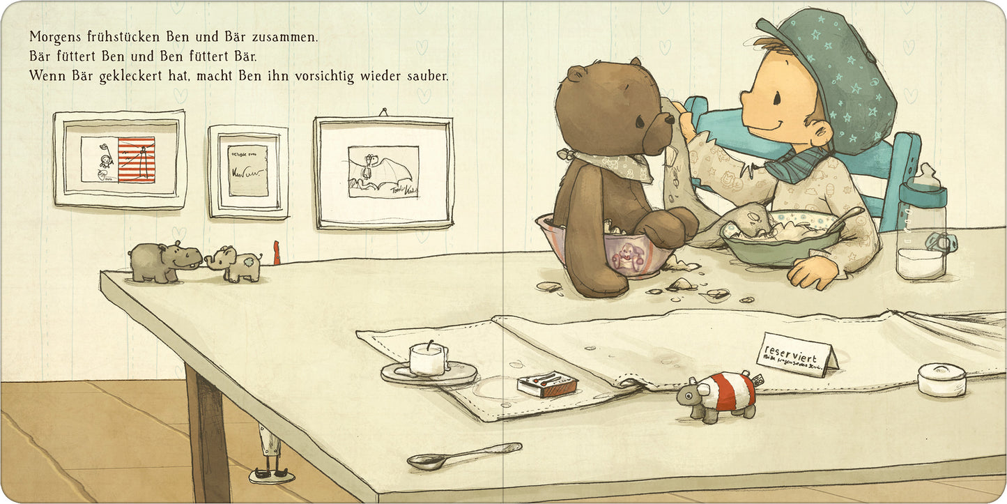 Gezeigt wird eine Innen- oder Zusatzansicht von „Ben liebt Bär ... und Bär liebt Ben“. In dieser Szene sitzen ein Junge namens Ben und ein brauner Teddybär an einem Tisch, umgeben von liebevollen Illustrationen. Der Tisch ist mit verschiedenen Frühstücksgegenständen, wie einer Tasse und einem Teller, dekoriert. An der Wand hängen Bilderrahmen mit kindlichen Zeichnungen. Die Farbpalette ist sanft und einladend, mit überwiegend Pastelltönen. Die Schrift ist klar und gut lesbar,...