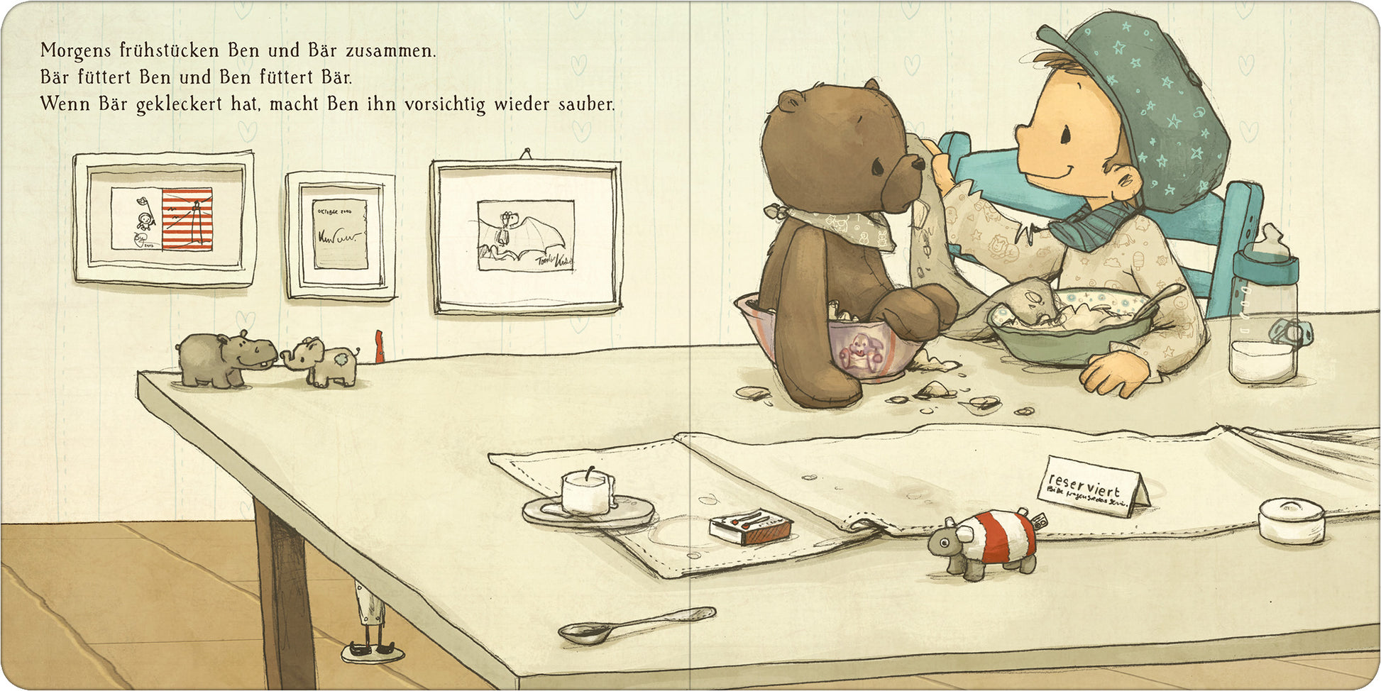 Gezeigt wird eine Innen- oder Zusatzansicht von „Ben liebt Bär ... und Bär liebt Ben“. In dieser Szene sitzen ein Junge namens Ben und ein brauner Teddybär an einem Tisch, umgeben von liebevollen Illustrationen. Der Tisch ist mit verschiedenen Frühstücksgegenständen, wie einer Tasse und einem Teller, dekoriert. An der Wand hängen Bilderrahmen mit kindlichen Zeichnungen. Die Farbpalette ist sanft und einladend, mit überwiegend Pastelltönen. Die Schrift ist klar und gut lesbar,...