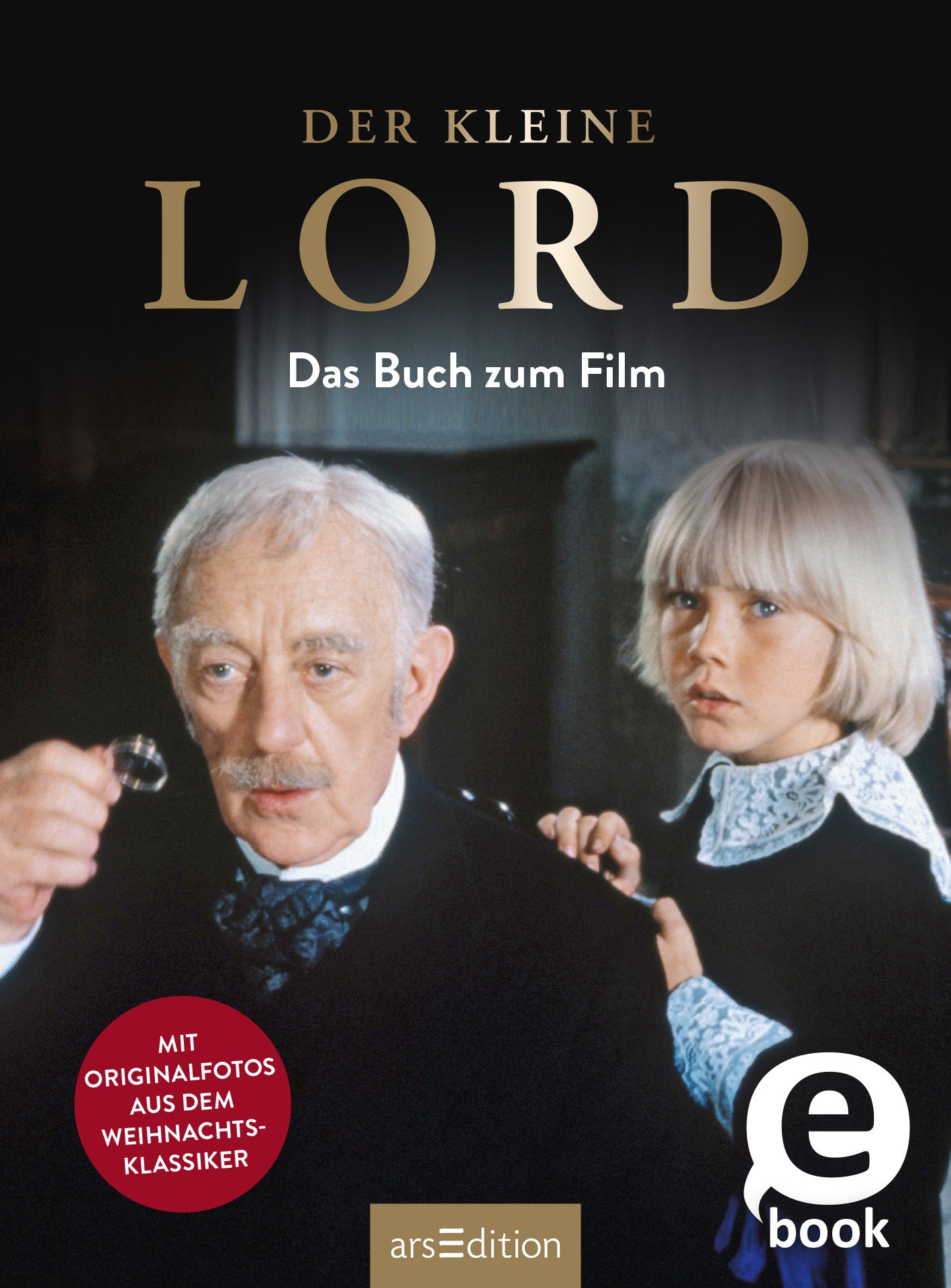Das Cover zeigt zwei Protagonisten aus dem Film „Der kleine Lord“. Links ist ein älterer Mann mit grauen Haaren und einem Anzug zu sehen, der eine kleine Uhr in der Hand hält. Rechts steht ein blondes Kind mit einem weißen Hemd und einem schwarzen Kragen. Der Titel „DER KLEINE LORD“ ist in großen goldenen Buchstaben oben platziert, darunter steht „Das Buch zum Film“ in schlichter Schrift. In der unteren linken Ecke befindet sich ein roter Button mit dem Text „MIT ORIGINALFOTOS...