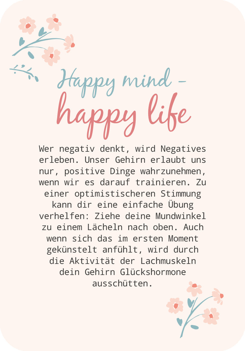 Gezeigt wird eine Innen- oder Zusatzansicht von „Glücksmantras für dich“. Die Seite präsentiert den Titel „Happy mind - happy life“ in einer verspielten, zweigeteilten Typografie: der erste Teil in sanftem Blau, der zweite in einem warmen Rosa. Darunter folgt ein erläuternder Text in einer klaren, gut lesbaren Schriftgröße auf hellem Hintergrund, umrahmt von zarten Blumenillustrationen in Pastelltönen, die eine positive und einladende Stimmung erzeugen.