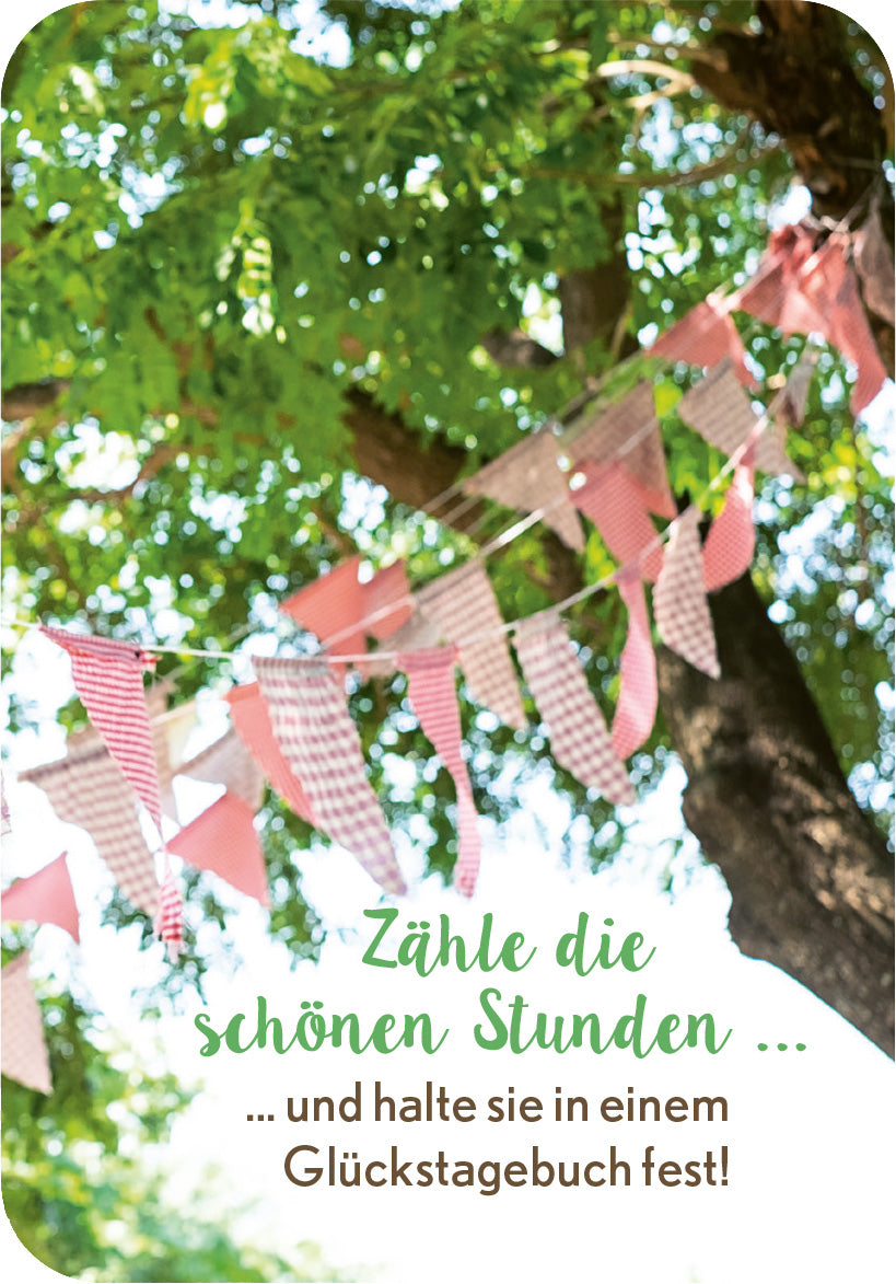 Gezeigt wird eine Innen- oder Zusatzansicht von „Achtsamkeit fürs Büro“. Das Bild zeigt eine entspannte, natürliche Umgebung mit einem großen Baum und bunten Wimpeln, die an einem Band befestigt sind. Die Wimpel sind in sanften Farben wie Rosa und Beige gehalten und schaffen eine fröhliche Stimmung. Der Schriftzug „Zähle die schönen Stunden ...“ ist in einer geschwungenen, grünen Schriftart gestaltet, während der Zusatztext „... und halte sie in einem Glückstagebuch fest!“...