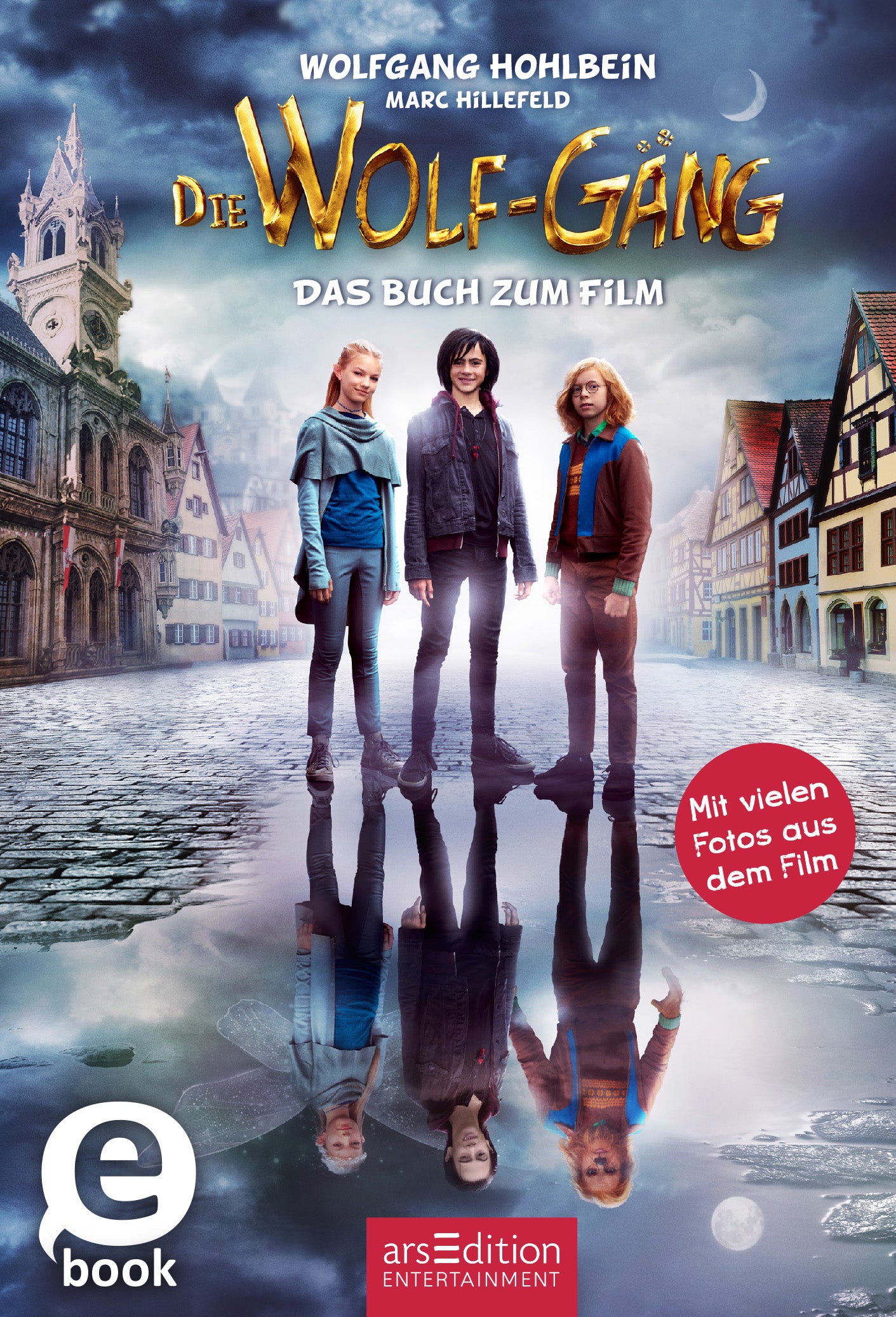 Das Buchcover zeigt drei jugendliche Figuren, die auf einem mystischen, nebligen Platz stehen, umgeben von historischen Gebäuden. Die Farbpalette umfasst gedämpfte Blau- und Brauntöne, die eine geheimnisvolle Atmosphäre schaffen. Der Titel „Die WOLF-GANG“ ist in goldener Schrift hervorgehoben, darunter steht „DAS BUCH ZUM FILM“. Ein roter Button weist auf „Mit vielen Fotos aus dem Film“ hin. Ganz unten mittig steht der Logoschriftzug von arsEdition.