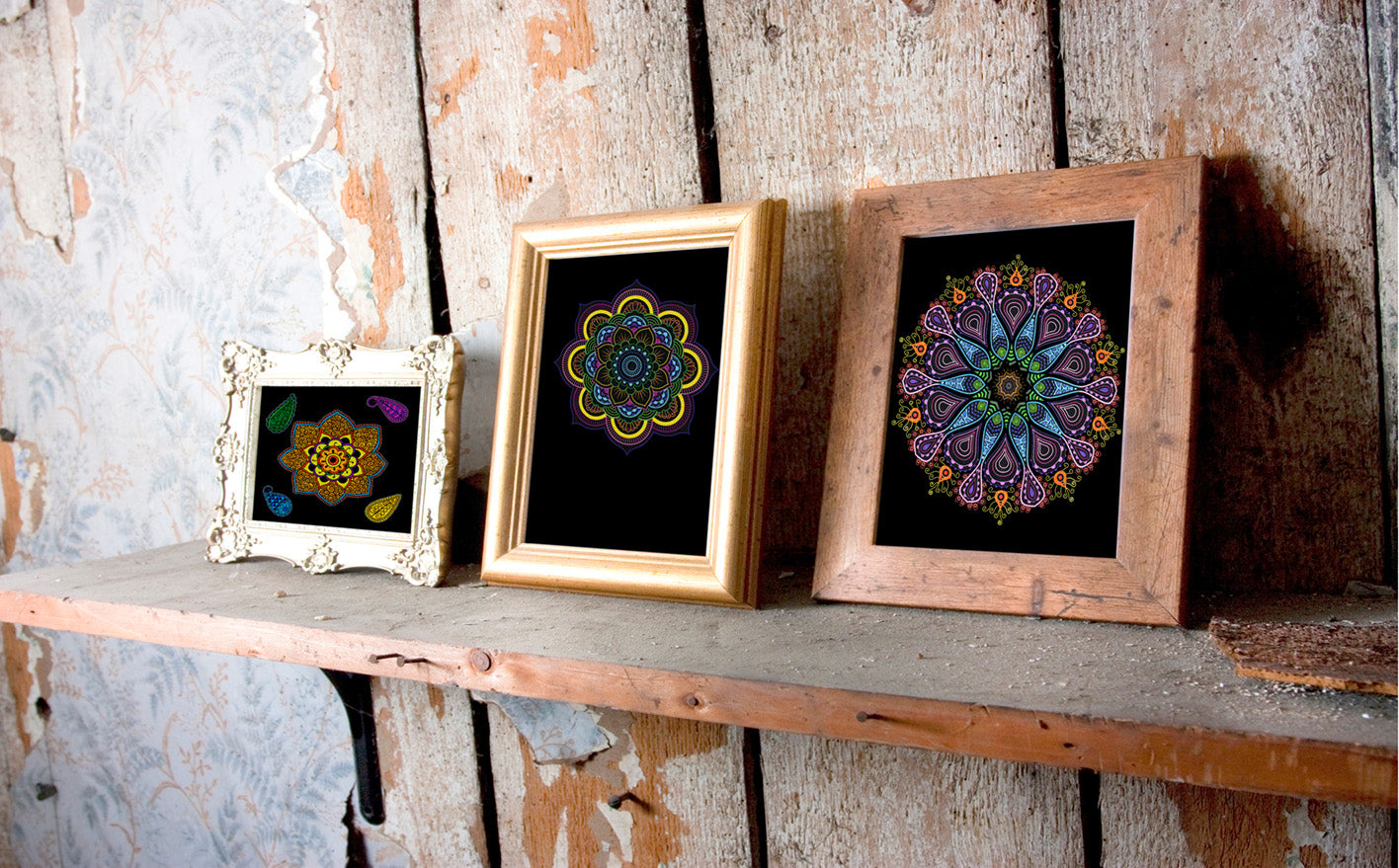 Gezeigt wird eine Innen- oder Zusatzansicht von „Mandala-Zauber“. Drei Rahmen mit farbenfroh ausgemalten Mandala-Motiven stehen auf einem Holzregal. Die Mandalas sind in leuchtenden Farben wie Blau, Gelb und Lila auf schwarzem Hintergrund gestaltet, während die Rahmen unterschiedlich sind: ein filigran verzierter weißer Rahmen, ein schlichter goldfarbener Rahmen und ein rustikaler Holzrahmen. Das Regal hängt an einer rustikalen Holzwand.