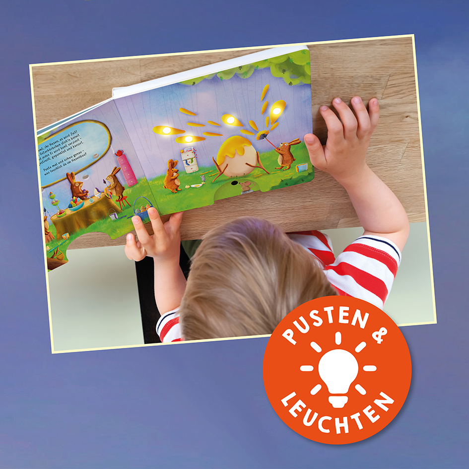 Gezeigt wird eine Innen- oder Zusatzansicht von „Mein liebstes Pustebuch – Träum schön!“. Auf der Abbildung sieht man ein Kind, das ein bunt illustriertes Bilderbuch auf einem Tisch betrachtet. Die Seiten sind in sanften Farben gehalten, mit dominierenden Grüntönen und fröhlichen Tierfiguren. Ein orangefarbenes Symbol mit der Aufschrift „Pustet & Leuchten“ ist in der Ecke platziert. Die Leseschrift ist deutlich und kindgerecht gestaltet.