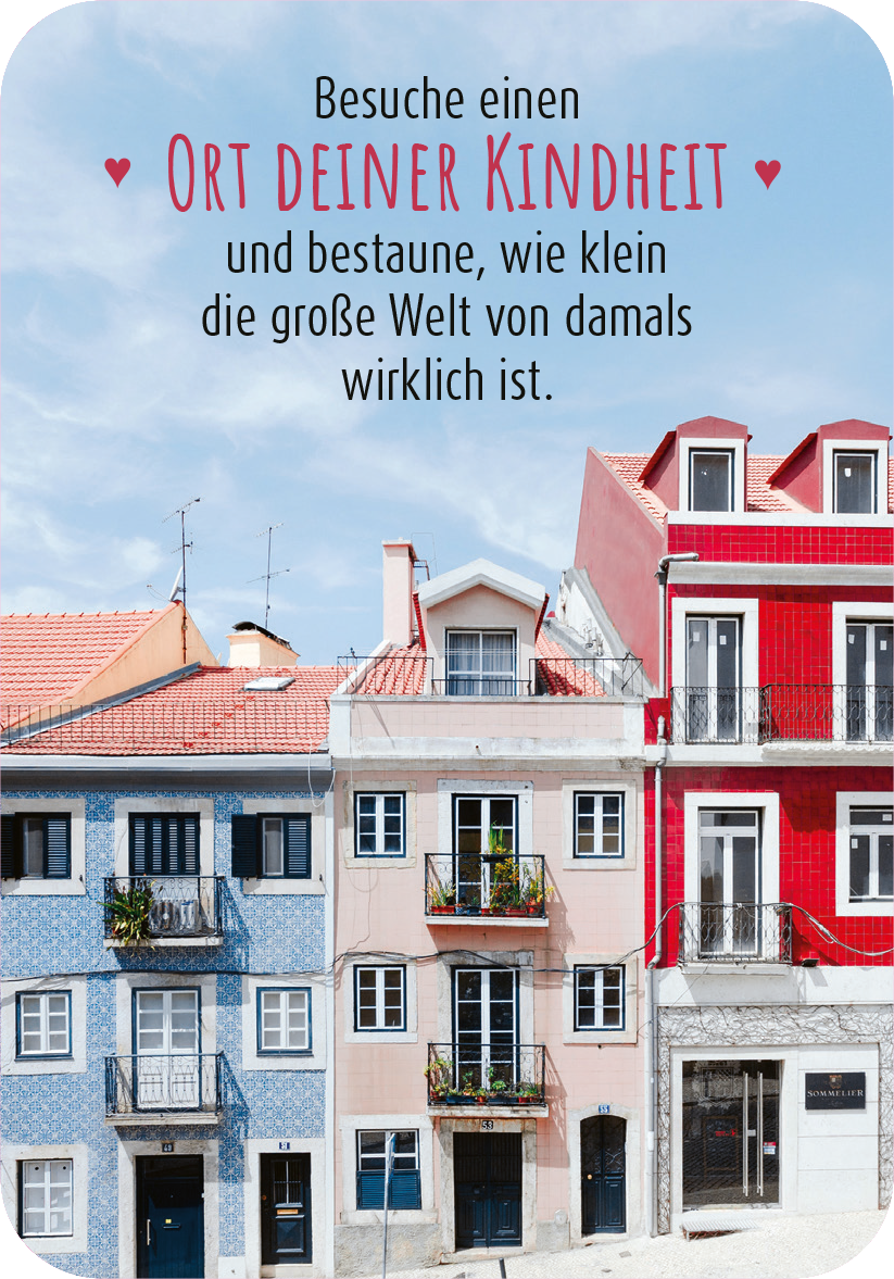 Gezeigt wird eine Innen- oder Zusatzansicht von „99 herrliche Auszeiten für zwischendurch“. Die Ansicht zeigt bunte, sanierte Häuserfassaden in Pastellfarben, darunter Blau, Rot und Weiß. Über den Gebäuden ist der handschriftliche Text „Besuche einen Ort deiner Kindheit und bestaune, wie klein die große Welt von damals wirklich ist“ in dunkler Schrift auf hellem Hintergrund platziert. Die Schrift ist verspielt und gut lesbar, was eine freundliche Atmosphäre vermittelt.