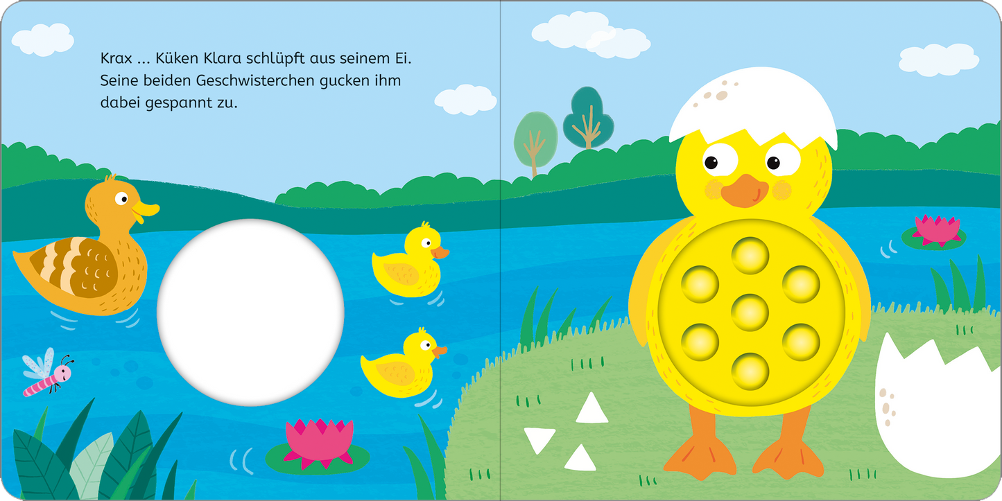 Gezeigt wird eine Innen- oder Zusatzansicht von „Mein erstes Pop-it-Buch – Küken Klara“. Die bunte Illustration zeigt Küken Klara, das aus einem Ei schlüpft, umgeben von zwei Geschwistern. Im Hintergrund erstreckt sich ein blauer See mit grünen Wiesen und bunten Blumen. Die Verwendung von leuchtenden Farben wie Gelb, Blau und Grün schafft eine fröhliche Atmosphäre. Die Schrift ist klar und gut lesbar, mit einfachem, kindgerechtem Text.