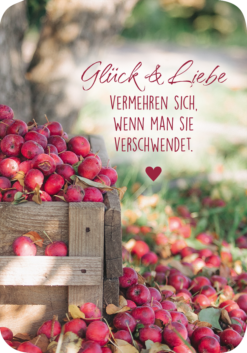 Gezeigt wird eine Innen- oder Zusatzansicht von „Weisheiten für die Seele“. Im Vordergrund befindet sich eine Holzkiste, gefüllt mit leuchtend roten Äpfeln. Der Hintergrund zeigt unscharf grünes Laub und einen baumartigen Schatten. In elegant geschwungener, roter Schrift steht der Text „Glück & Liebe“ über einem Zitat, das in einer klaren, schwarzen Schrift gewählt ist. Ein rotes Herz ergänzt das Design. Die Gesamtkomposition wirkt warm und einladend.