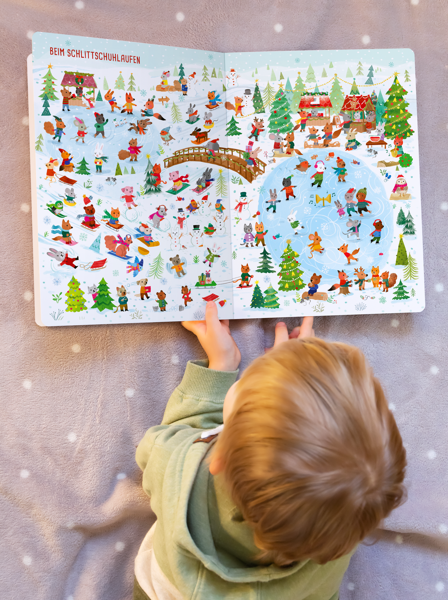 Gezeigt wird eine Innen- oder Zusatzansicht von „Mein großes Wimmelbuch – Im Winter“. Die Doppelseite zeigt eine winterliche Szene mit bunten Illustrationen von Menschen auf Schlittschuhen, die um einen gefrorenen Teich herum aktiv sind. Schneebedeckte Bäume und kleine Hütten sind prominent im Hintergrund. Die Farben sind lebendig und vielfältig, mit Blau- und Grüntönen sowie akzentuiertem Rot. Die Schrift „BEIM SCHLITTSCHUHLAUFEN“ ist in großer, roter Typografie oben links...