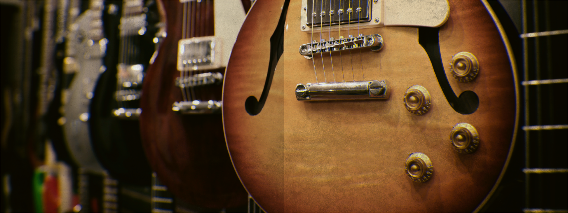 Gezeigt wird eine Innen- oder Zusatzansicht von „Ein Toter zur Bescherung“. Die Abbildung zeigt eine Reihe von Gitarren in verschiedenen Farben, darunter Holznuancen, Schwarz und Metallic-Töne. Im Vordergrund ist eine akustische Gitarre mit einer warmen, hellen Holzoberfläche zu sehen, die sanfte Kurven und ein glänzendes Finish aufweist. Die Beschläge und Mechaniken sind in Silber gehalten. Der Hintergrund ist verschwommen und zeigt weitere Instrumente, die die Vielfalt des Angebots...