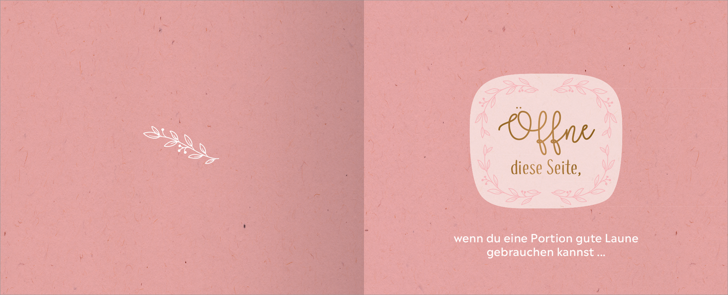 Gezeigt wird eine Innen- oder Zusatzansicht von „Happy Birthday – Alles Gute!“. Die doppelseitige Ansicht präsentiert einen sanften, rosa Hintergrund mit einer dezenten, strukturierten Optik. Links steht eine filigrane weiße Illustration einer Pflanze. Rechts befindet sich in einem abgerundeten, hellen Rahmen der Text „Offne diese Seite,“ in eleganter, goldfarbener Schrift, darunter steht in klarer, weißer Schrift „wenn du eine Portion gute Laune gebrauchen kannst…“.