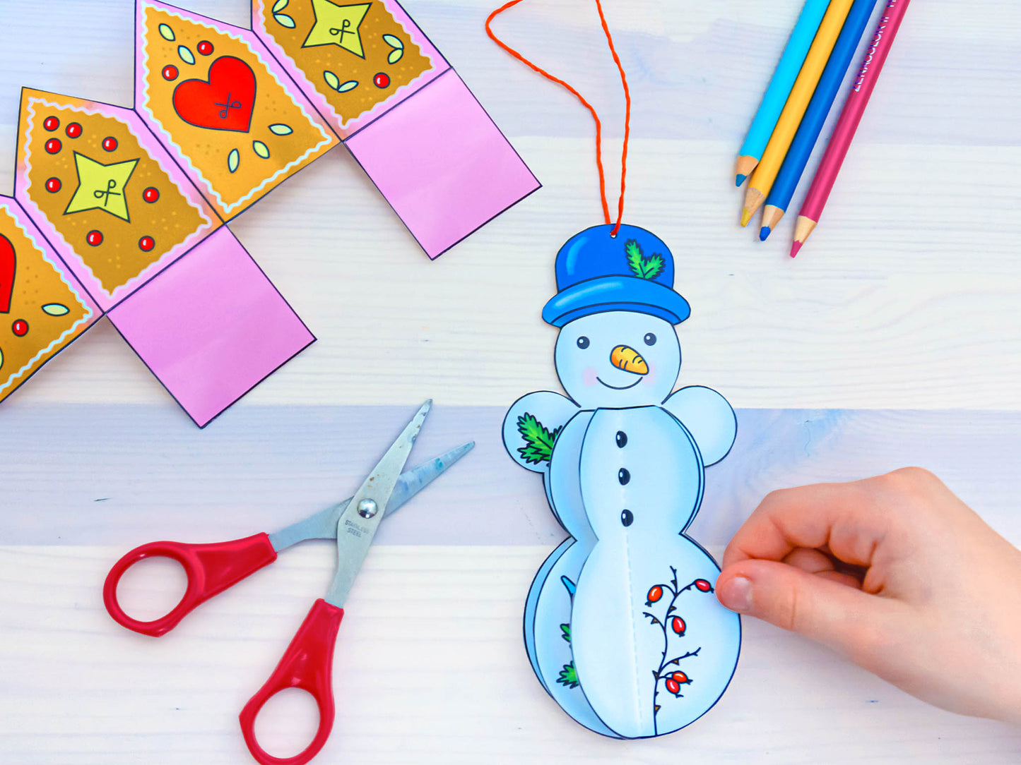 Gezeigt wird eine Innen- oder Zusatzansicht von „Mein erstes großes Winter-Bastelheft“. Die Abbildung zeigt verschiedene Bastelmaterialien auf einem hellen Tisch. Im Fokus liegt ein giebelförmiges Weihnachtsgebäude in lebhaften Farben mit Herzmustern. Ein fröhlicher Schneemann in Blau und Weiß wird gerade mit einer Hand gehalten, während eine Schere in der anderen Hand ruht. Bunte Buntstifte in verschiedenen Farben sind im Hintergrund sichtbar. Die freundliche, kinderfreundliche...