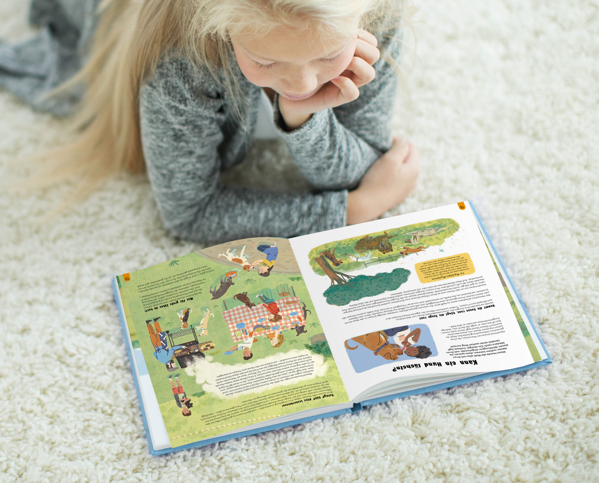 Gezeigt wird eine Innen- oder Zusatzansicht von „Die Welt der Hunde“. Die Doppelseite zeigt lebendige Illustrationen und ansprechende Farben, darunter sanfte Grüntöne und warme Erdtöne. Auf der linken Seite sind Kinder und Hunde abgebildet, die in einer Freizeitaktivität dargestellt werden. Die rechte Seite enthält Text, der in gut lesbarer, klarer Schriftart angeordnet ist, ergänzt durch visuelle Elemente, die das Thema Hundefreundschaft unterstützen.