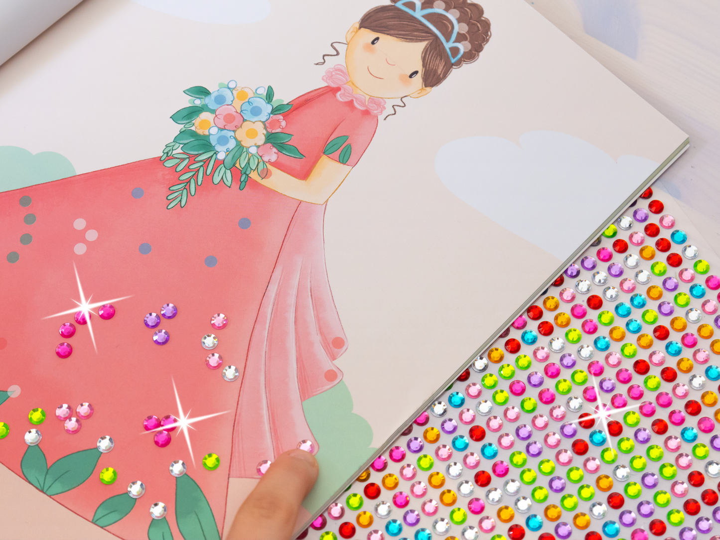 Gezeigt wird eine Innen- oder Zusatzansicht von „Diamantsticker Anziehpuppen – Prinzessinnen und Prinzen“. Die Szene zeigt ein illustriertes Mädchen in einem pinken Kleid, das einen Blumenstrauß hält. Auf der linken Seite sind bereits aufgeklebte, funkelnde Diamantsticker in verschiedenen Farben und Formen zu sehen, darunter Pink und Lila. rechts befindet sich ein Bogen mit vielen bunten Diamantstickern, die auf weißem Hintergrund angeordnet sind. Die illustrative Schrift ist...