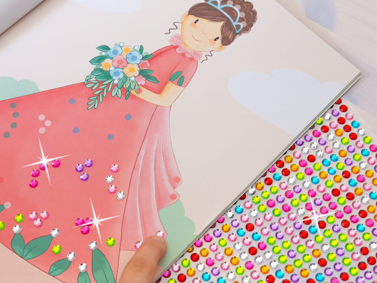 Gezeigt wird eine Innen- oder Zusatzansicht von „Diamantsticker Anziehpuppen – Prinzessinnen und Prinzen“. Die Szene zeigt ein illustriertes Mädchen in einem pinken Kleid, das einen Blumenstrauß hält. Auf der linken Seite sind bereits aufgeklebte, funkelnde Diamantsticker in verschiedenen Farben und Formen zu sehen, darunter Pink und Lila. rechts befindet sich ein Bogen mit vielen bunten Diamantstickern, die auf weißem Hintergrund angeordnet sind. Die illustrative Schrift ist...