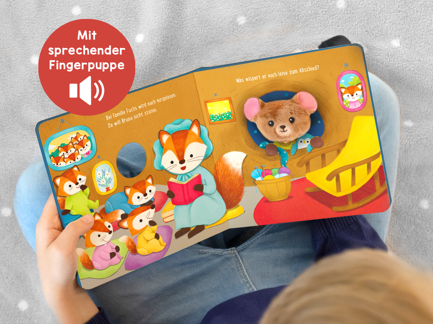 Gezeigt wird eine Innen- oder Zusatzansicht von „Meine sprechende Fingerpuppe: Was sagt der Bär?“. Die Illustration zeigt eine bunte Szenerie mit einem Fuchs in blauer Kleidung, der ein Buch liest, umgeben von weiteren Tieren. Die Farben sind lebhaft, dominierend sind warme Rottöne, sanfte Blautöne und erdige Gelbtöne. Die Typografie ist freundlich und kindgerecht, mit einer klaren Lesbarkeit. Ein Symbol mit dem Hinweis „Mit sprechender Fingerpuppe“ ist oben links platziert.