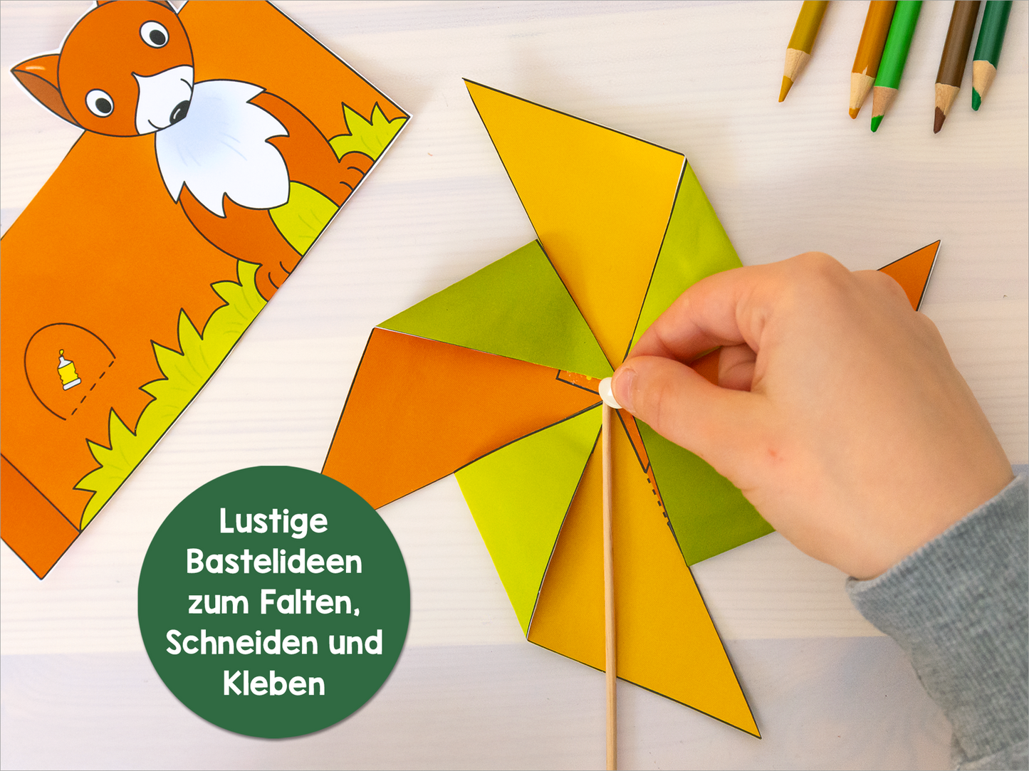 Gezeigt wird eine Innen- oder Zusatzansicht von „Mein erstes großes Herbst-Bastelheft“. Auf dem Bild sind farbenfrohe Bastelideen zu sehen, darunter eine Hand, die ein buntes, faltbares Bastelobjekt in Form eines Windrads hält. Die Farben reichen von leuchtendem Gelb bis zu frischem Grün. Im Hintergrund ist eine stilisierte Zeichnung eines kleinen Fuchses und einer Wiese. Der Text in einem grünen Kreis lautet: „Lustige Bastelideen zum Falten, Schneiden und Kleben“.