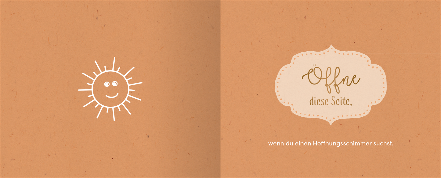 Gezeigt wird eine Innen- oder Zusatzansicht von „Kopf hoch – Alles wird wieder gut“. Die Seite zeigt einen warmen, orangefarbenen Hintergrund. Auf der linken Seite ist ein fröhliches, einfaches Sonnengesicht in Weiß abgebildet. Auf der rechten Seite steht der Text „Öffne diese Seite,“ in einer verschnörkelten, handschriftlichen Schriftart, umrahmt von einem eleganten, hellen Banner mit einem geschwungenen Rand. Darunter folgt die Aufforderung „wenn du einen Hoffnungsschimmer...