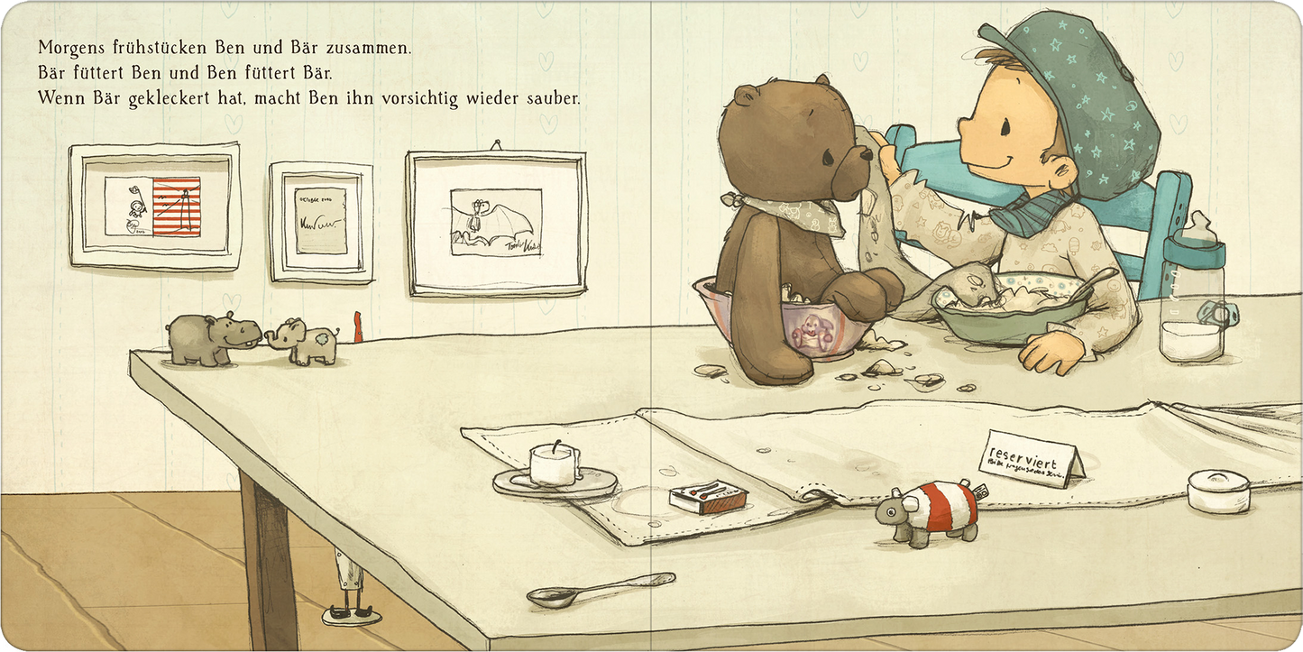 Gezeigt wird eine Innen- oder Zusatzansicht von „Die schönsten Geschichten von Ben und Bär“. Die Illustration zeigt Ben, ein kleiner Junge mit blauer Mütze und gestreiftem Pullover, der liebevoll seinen Teddy Bär füttert. Im Hintergrund hängen Bilderrahmen mit einfachen Zeichnungen an der Wand. Die Farbpalette ist sanft und warm, dominiert von Beige- und Brauntönen. Auf dem Tisch sind Frühstücksreste und Spielzeug zu sehen, was eine gemütliche, einladende Atmosphäre schafft.