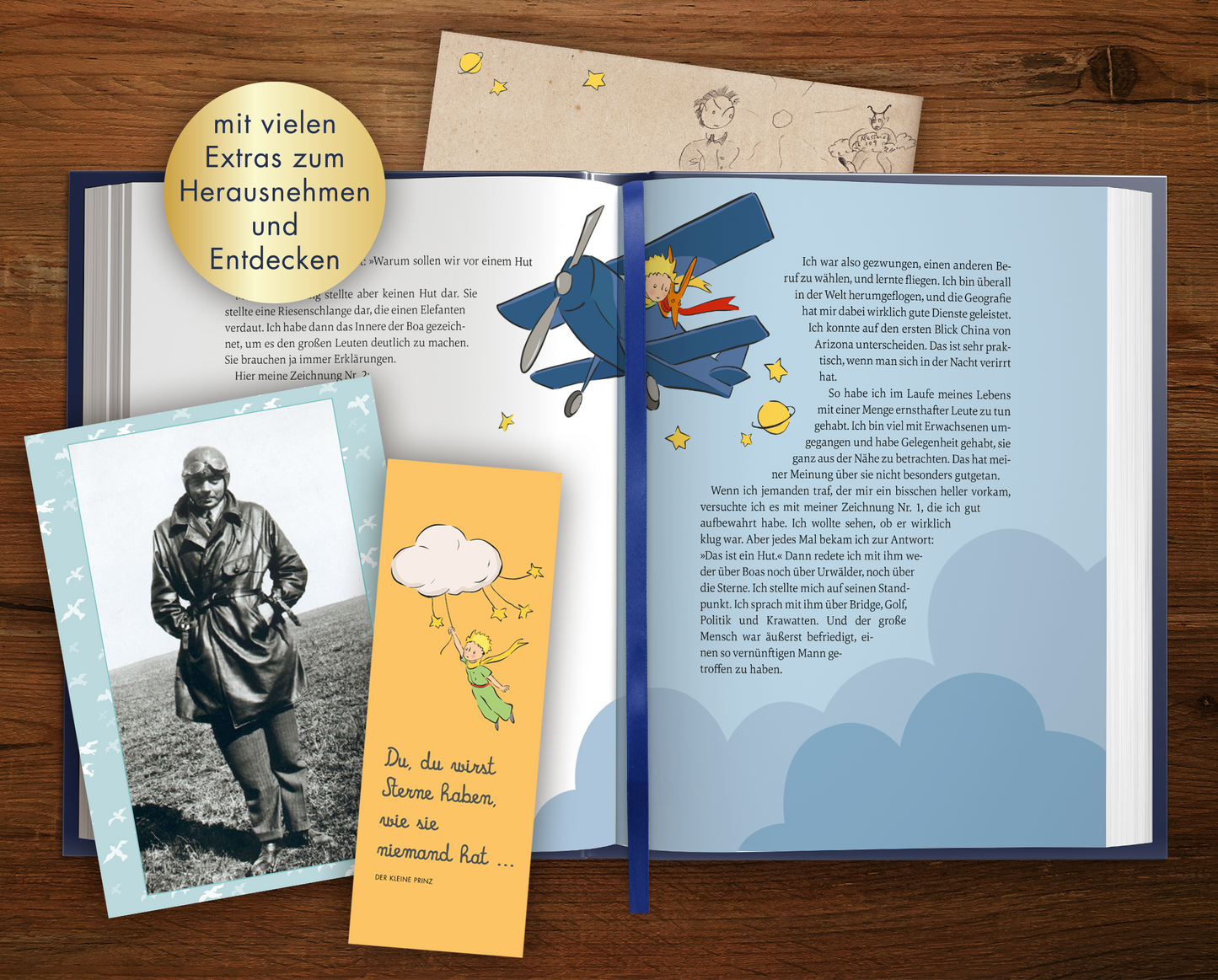 Gezeigt wird eine Innen- oder Zusatzansicht von „Der Kleine Prinz“. Die Seiten zeigen sanfte Blautöne mit Illustrationen des kleinen Prinzen in seinem Flugzeug, umgeben von gelben Sternen. Auf der linken Seite befindet sich ein nostalgisches Foto eines Mannes in einem Anzug sowie zwei bunte, illustrative Extras zum Herausnehmen. Eine der Beigaben zeigt einen stilisierten Wolkenhimmel mit dem Text: „Die du wert bist...“. Die Typografie ist abwechslungsreich und versprüht einen...