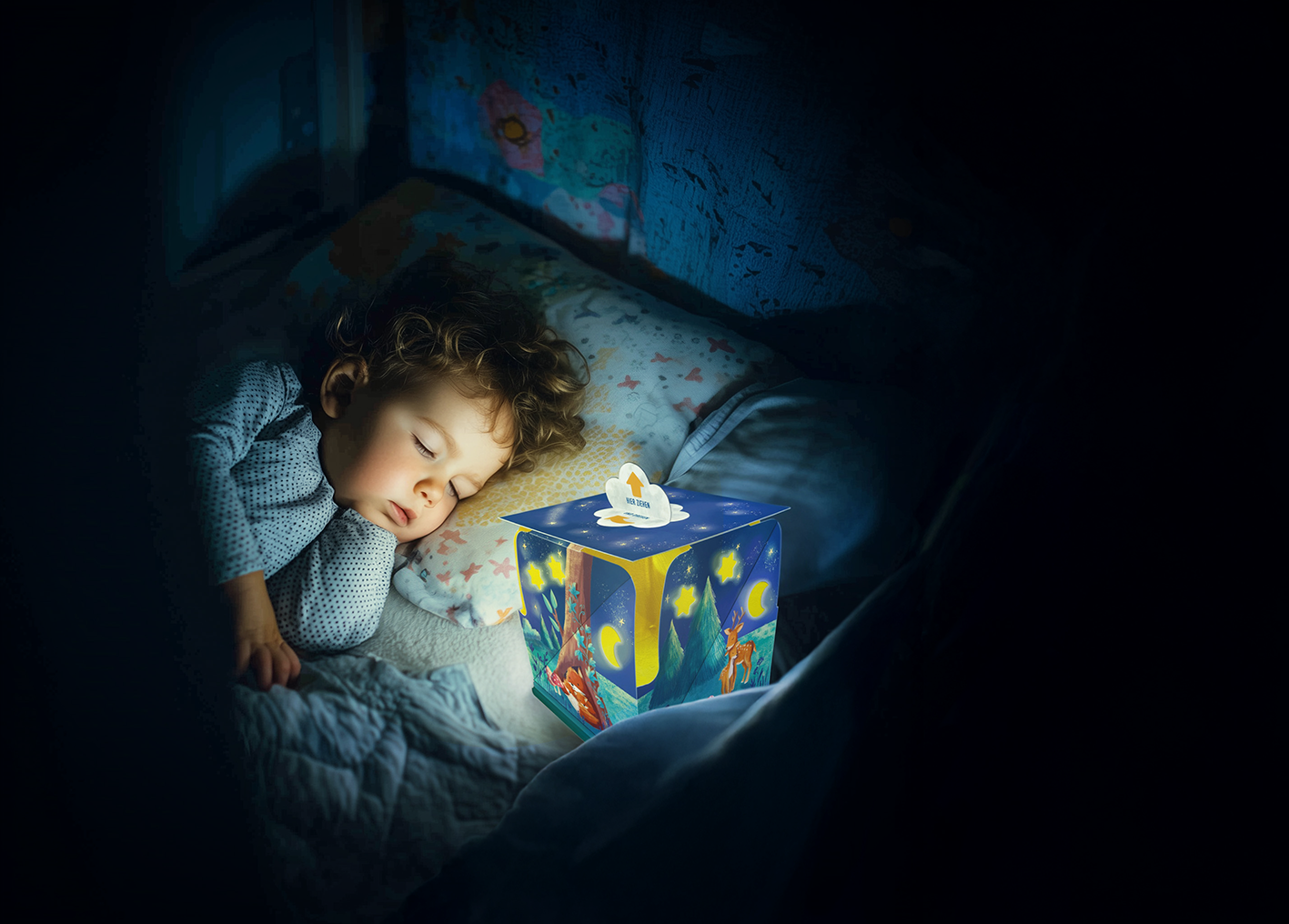 Gezeigt wird eine Innen- oder Zusatzansicht von „Ich schenk dir ein Licht! Schlaf, Kindlein, schlaf“. Im Vordergrund schläft ein kleines Kind auf einem Bett mit einem hellblauen Kissen. Neben dem Kind steht ein buntes Nachtlicht in Form eines Würfels, das zauberhafte Bilder zeigt. Die Farben des Lichtes sind hauptsächlich Blau und Gelb, die sanfte Atmosphäre schaffen. Die Typografie auf dem Nachtlicht ist kindgerecht und einladend gestaltet.