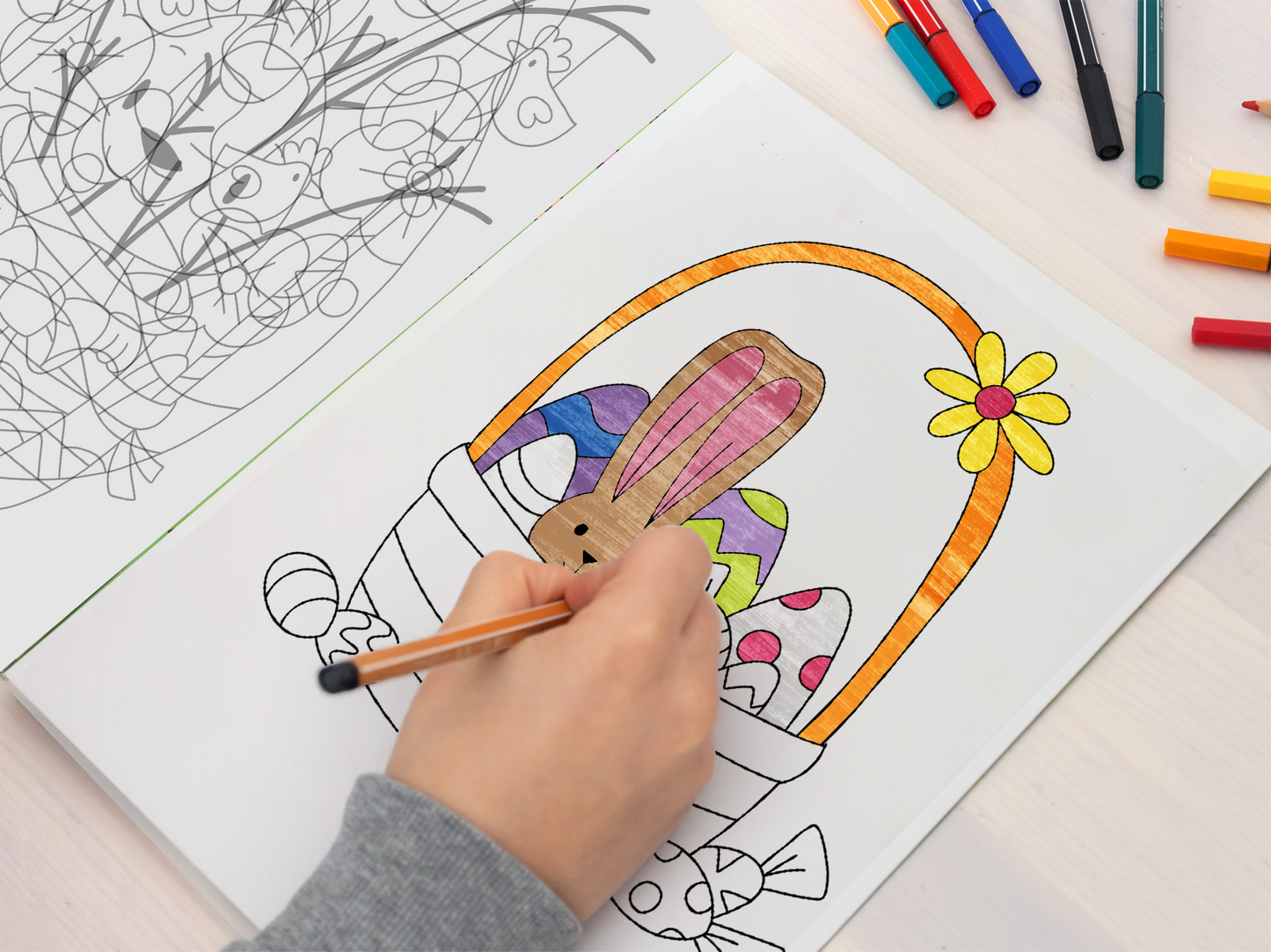 Gezeigt wird eine Innen- oder Zusatzansicht von „Ausmal-Fensterbilder Ostern“. Das Bild zeigt eine Illustratorin, die mit einem Buntstift ein Osternest ausmalt. Das Nest ist mit bunten Eiern, einem Hasen und einer Blume verziert, die in lebhaften Farben wie Blau, Gelb, Rosa und Lila strahlen. Der Hintergrund ist schlicht, wobei der Fokus auf dem Ausmalbild und der kreativen Tätigkeit liegt.