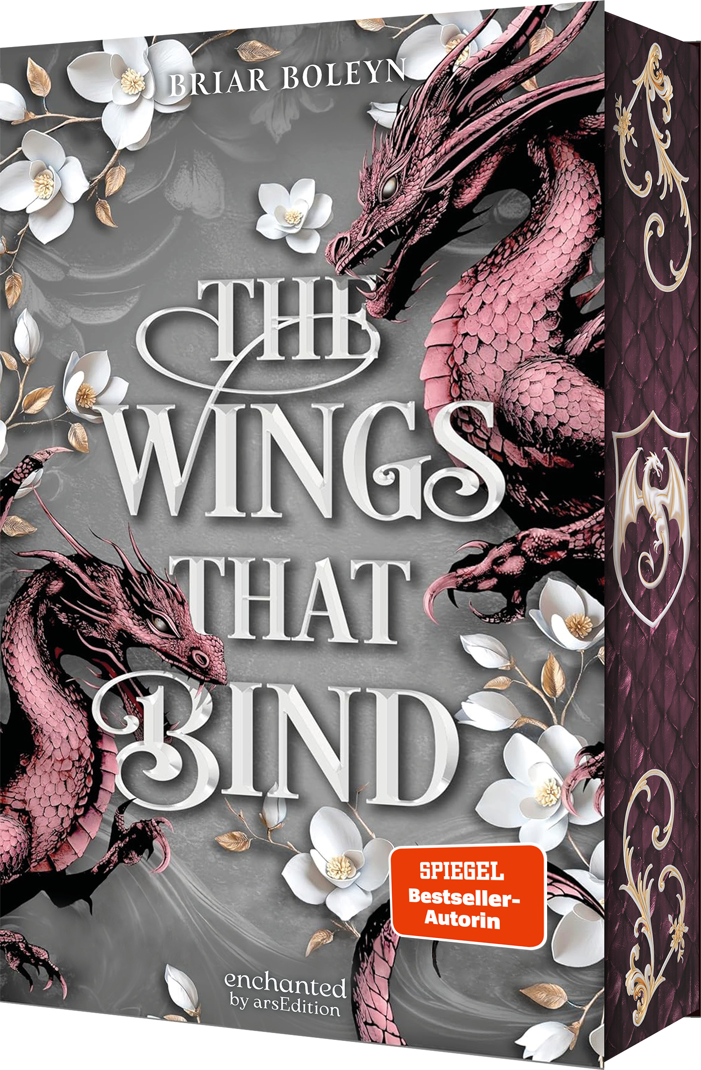 Das Buchcover zeigt zwei detailliert gestaltete Drachen in verschiedenen Rottönen, die vor einem dunklen, schlichten Hintergrund angeordnet sind. Umrahmt von zarten weißen Blüten strahlt das Cover eine mystische Atmosphäre aus. Der Name der Autorin Briar Boleyn steht ganz oben. Der Titel „THE WINGS THAT BIND“ ist in großen, eleganten Buchstaben in der Mitte platziert. In der unteren rechten Ecke befindet sich ein orangefarbener Button mit dem Text „SPIEGEL Bestseller-Autorin“. Ganz...