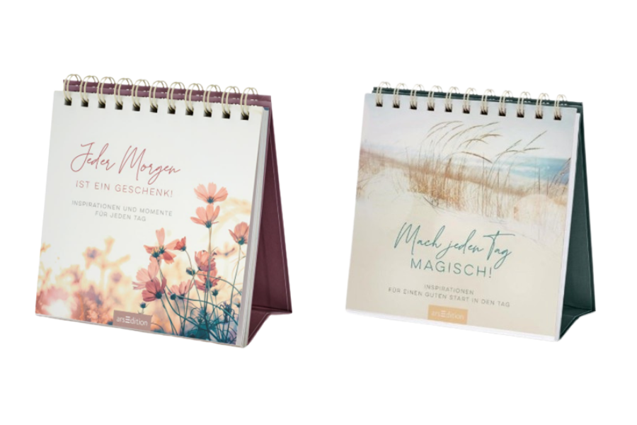 Zwei Spiral-Tischkalender aufgestellt. Der linke Kalender trägt den Titel „Jeder Morgen ist ein Geschenk!“ mit einem floralen Motiv. Der rechte Kalender zeigt den Titel „Mach jeden Tag magisch!“ mit einer Landschaft aus Dünen und Gräsern. Beide bieten tägliche Inspirationen und motivierende Zitate.