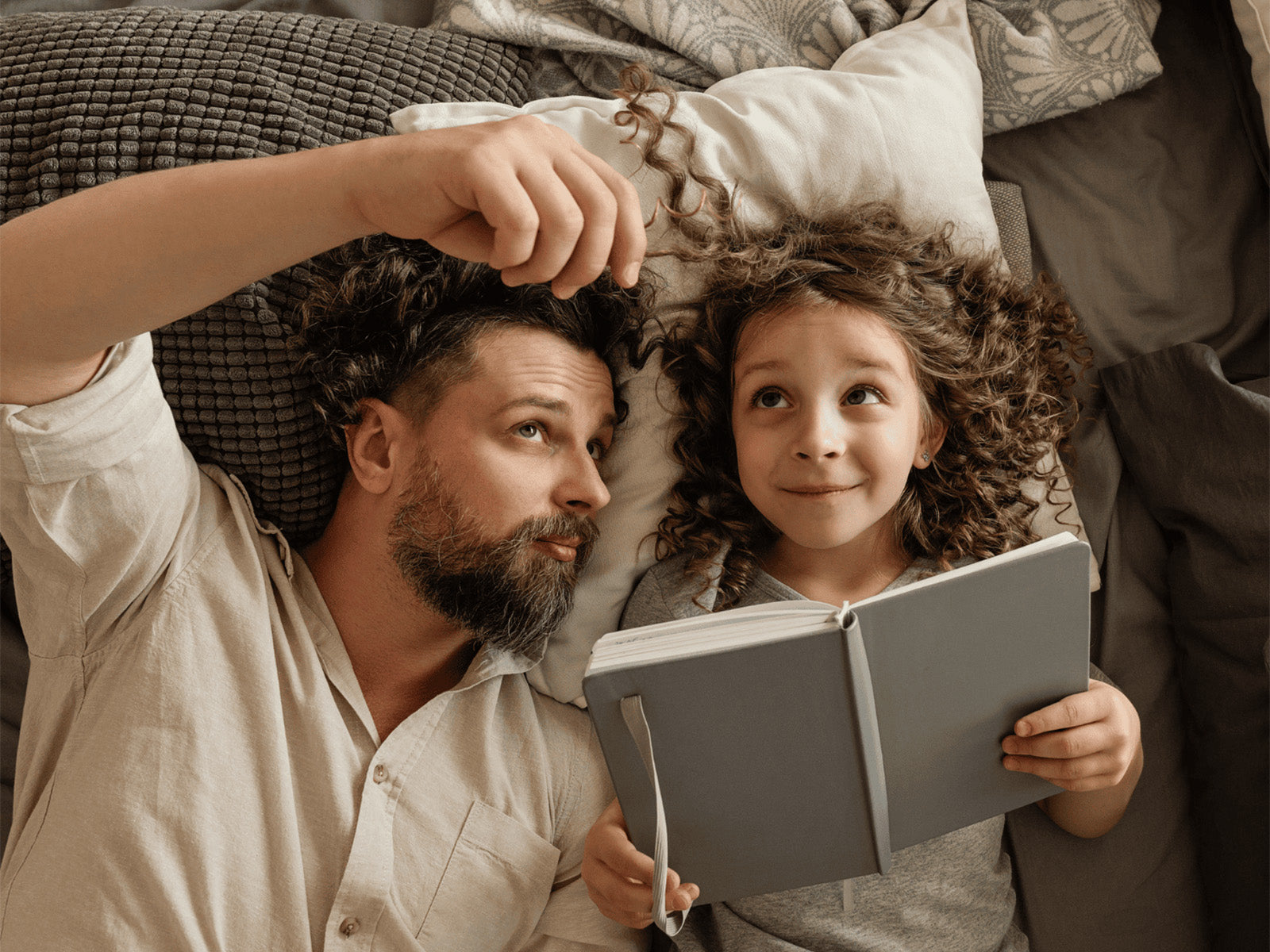 Ein junges Mädchen liegt mit ihrem Papa auf dem Bett. Beide lesen ein Buch.