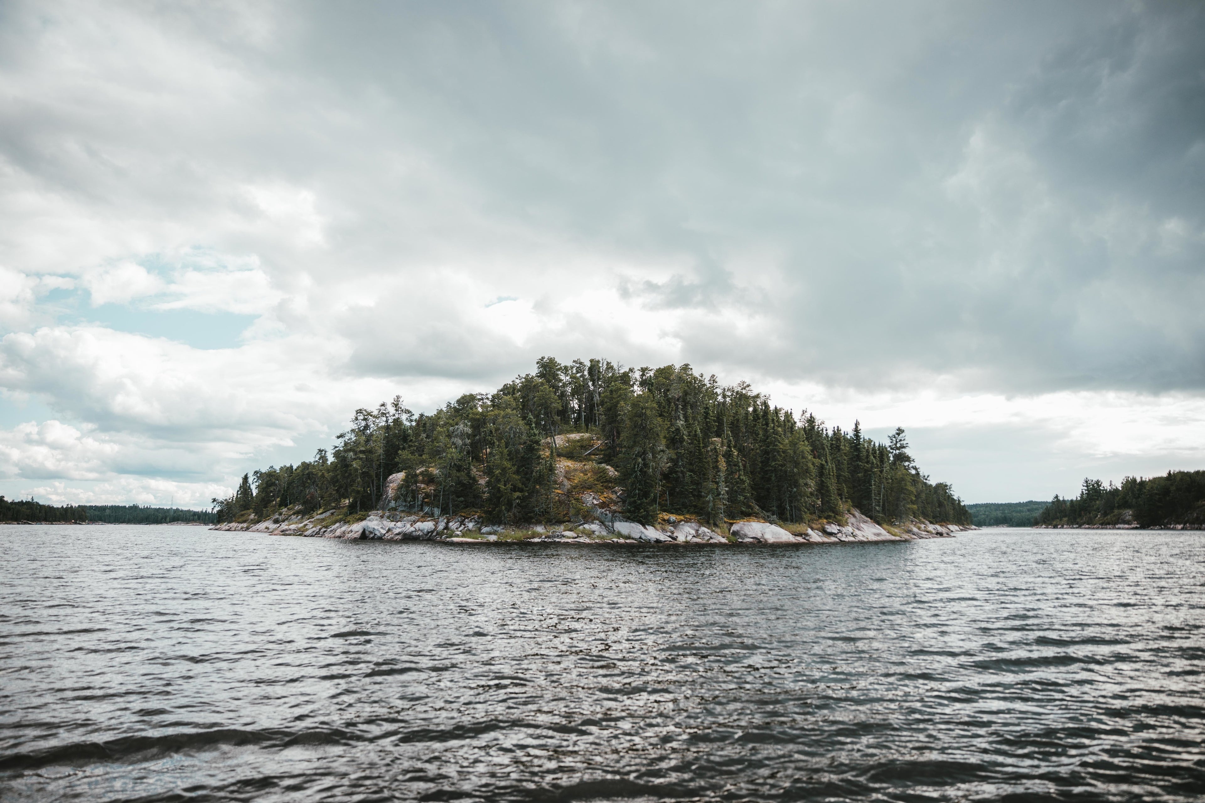 Eine kleine bewaldete Insel inmitten eines Sees, umgeben von ruhigem Wasser.