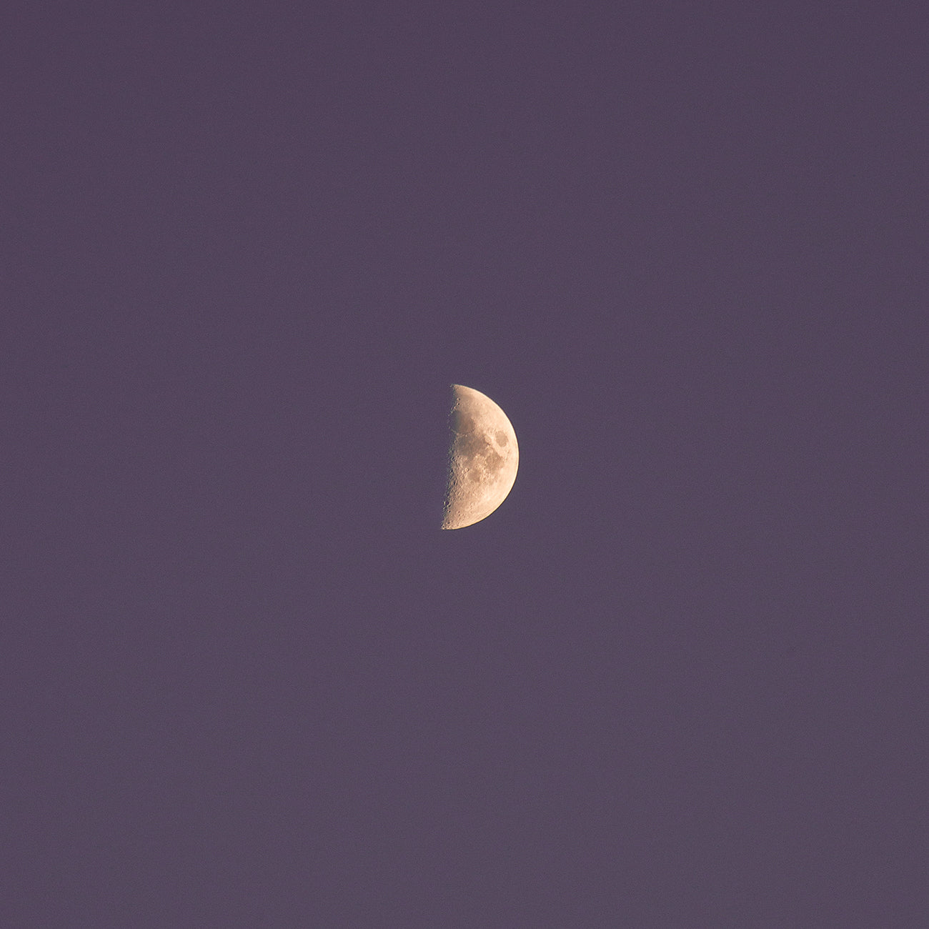 Halbmond am Nachthimmel mit klaren Details der Mondoberfläche, umgeben von einem violetten Himmel.