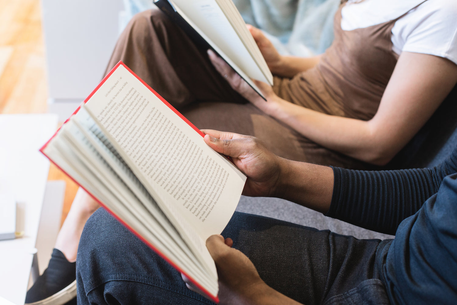 Zwei Personen sitzen nebeneinander und lesen Bücher. Die Szene zeigt Hände, die Bücher halten, mit einem Fokus auf das Lesen in einer ruhigen Umgebung.