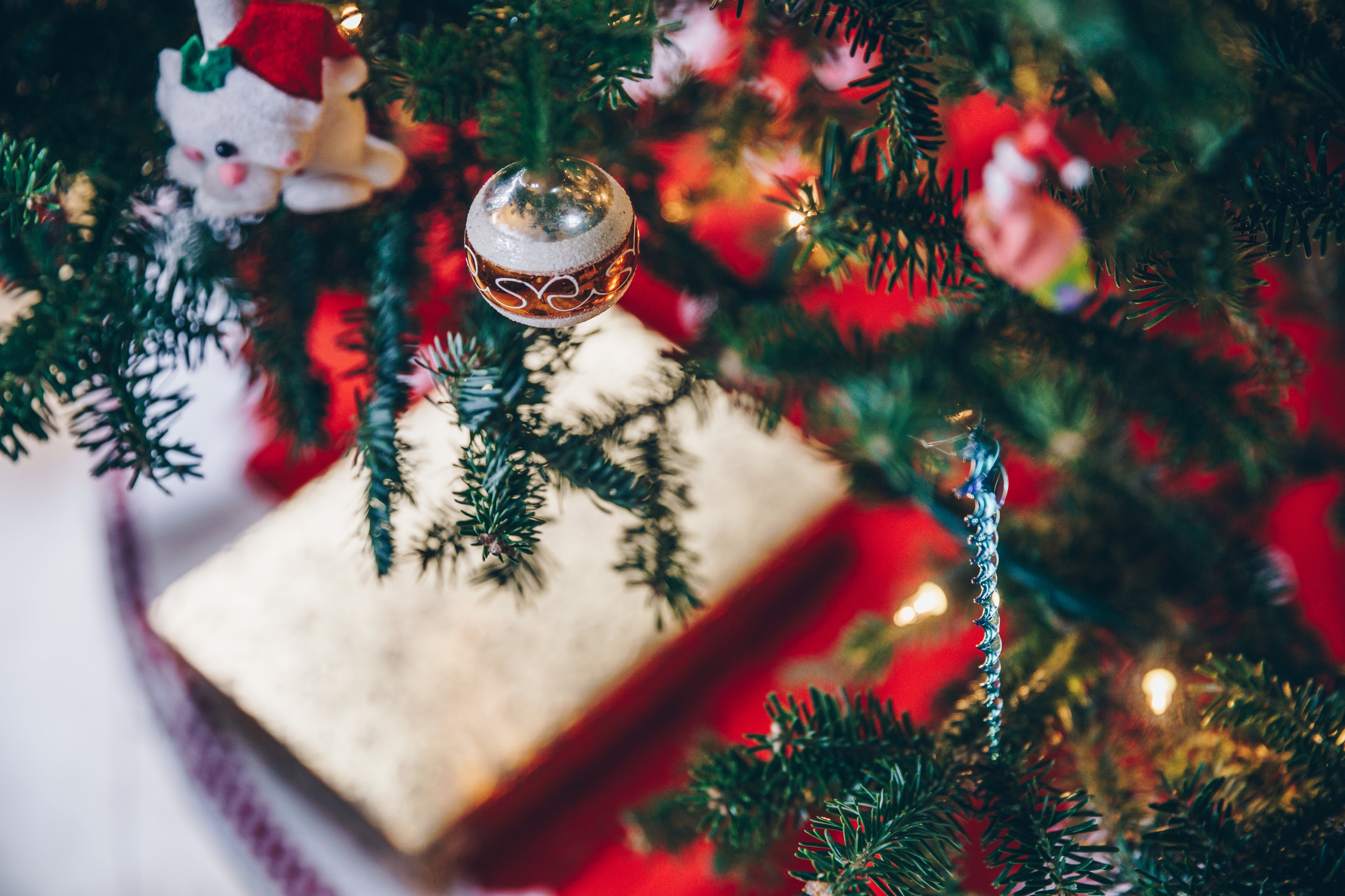 Nahaufnahme eines geschmückten Weihnachtsbaums mit grünen Tannenzweigen, einer silbernen Kugel und einer kleinen weißen Figur mit Weihnachtsmütze.