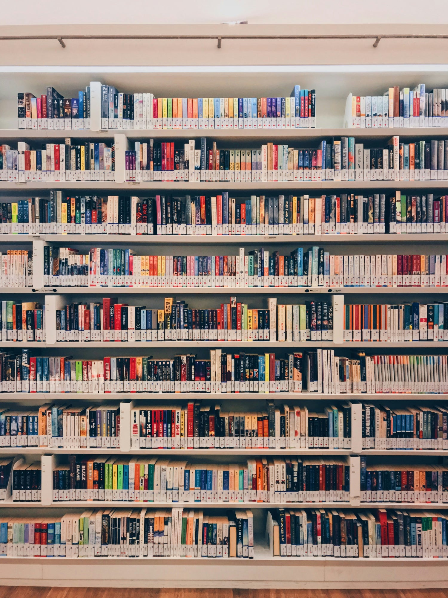 Foto eines großen Bücherregals in einer Bibliothek, gefüllt mit Büchern in verschiedenen Farben und Größen, die in mehreren Reihen ordentlich angeordnet sind. Die Bücher sind unterschiedlich kategorisiert und stehen vor einem hellen, modernen Hintergrund