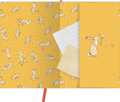 Gezeigt wird eine Innen- oder Zusatzansicht von „myNOTES Papeterie: Notizbuch A5 WDEWLIDH“. Die Seite ist in einem warmen Gelbton gestaltet und zeigt wiederkehrende, niedliche Hasen-Motive in verschiedenen Positionen. Ein in Weiß gehaltenes liniertes Blatt ist teilweise sichtbar, daneben liegt ein beige-farbenes Blatt. Rechts ist ein Hase abgebildet, der eine Blume in der Hand hält, umgeben von kleinen Schmetterlingen. Der Stil ist verspielt und ansprechend, mit einer freundlichen...
