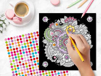 Gezeigt wird eine Innen- oder Zusatzansicht von „Diamond Mandalas“. Im Vordergrund ist eine bunte Mandala-Zeichnung auf schwarzem Hintergrund zu sehen, die mit verschiedenen Farben, darunter gelb, grün und rosa, verziert ist. Eine Hand hält einen gelben Stift und färbt die Zeichnung aus. Zudem sind bunte Dekosticker und pastellfarbene Macarons auf einem weißen Tisch sichtbar, sowie eine Tasse Kaffee im Hintergrund. DieTypografie wird durch stilisierte Schriftzüge ergänzt.