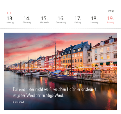 Gezeigt wird eine Innen- oder Zusatzansicht von „Postkartenkalender Fernwehmomente 2026“. Im Vordergrund ist ein malerischer Hafen mit Booten zu sehen, umgeben von bunten, historischen Gebäuden. Der Himmel ist in sanften Pastellfarben gehalten, die eine romantische Atmosphäre erzeugen. In der unteren Bildhälfte steht das Zitat „Für einen, der nicht weiß, welchen Hafen er ansteuert, ist jeder Wind der richtige Wind.“ in klarer, eleganter Schrift, darunter der Autorennamen Seneca.