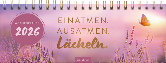 Auf dem Cover eines Wochenplaners für 2026 dominiert ein sanfter, pinker Farbverlauf im Hintergrund, durchzogen von lila Lavendelblüten. In der oberen Hälfte schwebt ein orangefarbener Schmetterling. Die Schriftzüge „EINATMEN. AUSATMEN. LÄCHELN.“ sind in eleganten, goldfarbenen Buchstaben gehalten. Oben links befindet sich ein runder Button mit dem Text „WOCHENPLANER 2026“. Ganz unten mittig steht der Logoschriftzug von arsEdition.