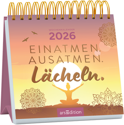 Der Wochenkalender „EINATMEN. AUSATMEN. Lächeln.“ für das Jahr 2026 präsentiert sich in sanften Pastellfarben mit einem harmonischen Verlauf von Orange zu Lila. In der Mitte ist eine meditierende Silhouette vor einer großen, stilisierten Sonne abgebildet. Dekorative Mandala-Elemente runden das Design ab. Die Schrift ist geschwungen und einladend. Ganz oben steht in Dezent der Hinweis „WOCHENKALENDER 2026“. Ganz unten mittig steht der Logoschriftzug von arsEdition.