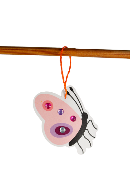 Gezeigt wird eine Innen- oder Zusatzansicht von „Diamant-Oster-Anhänger“. Der Anhänger zeigt die Form eines Schmetterlings in sanften Rosa- und Lilatönen. Er ist mit glitzernden Strasssteinen in verschiedenen Farben verziert. Der Körper des Schmetterlings ist schwarz abgegrenzt, während ein orangefarbener Faden oben befestigt ist. Der Hintergrund ist weiß, wodurch die Farben lebendig und ansprechend zur Geltung kommen.