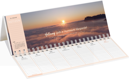 Gezeigt wird eine Innen- oder Zusatzansicht von „Tischkalender Lebensweisheiten 2027“. Der Kalender ist aufgeschlagen und präsentiert eine sanfte Farbpalette mit einem warmen Sonnenuntergang über einer Wolkendecke. Die oberhalb platzierte, geschwungene Schrift zitiert: „Hoffnung glüht in Sturm macht Margeriten!“. Der kalendarische Bereich ist übersichtlich strukturiert, mit klaren Linien und hellen Notizfeldern, die eine einfache Nutzung ermöglichen. Ein minimalistisches, modernes...