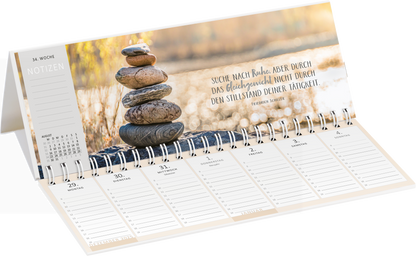 Gezeigt wird eine Innen- oder Zusatzansicht von „Tischkalender Einatmen. Ausatmen. Lächeln. 2027“. Die Gestaltung zeigt eine sanfte, helle Farbpalette mit Naturtönen und einer ruhigen Bildkomposition. Im oberen Bereich sind gestapelte Steine zu sehen, die Harmonie symbolisieren. Rechts daneben steht der inspirierende Spruch „Suche nach Ruhe, aber durch das Gleichgewicht nicht durch den Stillstand deiner Tätigkeiten“ in einer klaren, freundlichen Schrift. Unten sind die Wochentage mit...