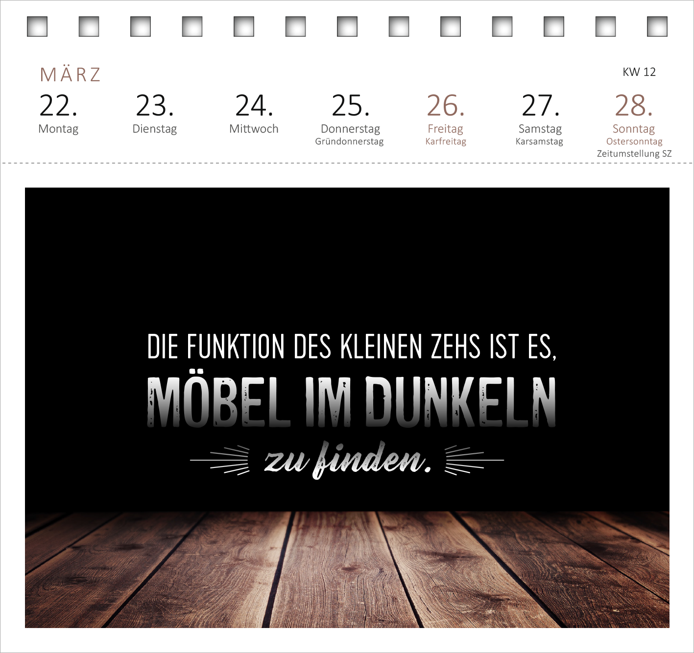 Gezeigt wird eine Innen- oder Zusatzansicht von „Postkartenkalender Meine Schokoladenseite hab ich aufgegessen. 2027“. Die Seite präsentiert einen schlichten, dunklen Hintergrund mit weißer und grauer Schrift. Der zentrale Text lautet: „DIE FUNKTION DES KLEINEN ZEHS IST ES, MÖBEL IM DUNKELN zu finden.“. Unter dem Text sind stilisierte, dekorative Linien zu sehen. Der untere Bereich wird durch eine warme Holzoberfläche ergänzt, die einen harmonischen Kontrast bildet.