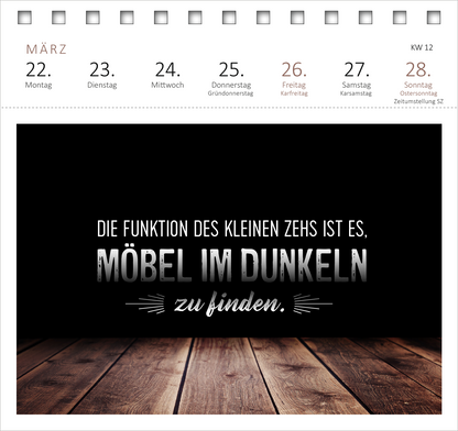 Gezeigt wird eine Innen- oder Zusatzansicht von „Postkartenkalender Meine Schokoladenseite hab ich aufgegessen. 2027“. Die Seite präsentiert einen schlichten, dunklen Hintergrund mit weißer und grauer Schrift. Der zentrale Text lautet: „DIE FUNKTION DES KLEINEN ZEHS IST ES, MÖBEL IM DUNKELN zu finden.“. Unter dem Text sind stilisierte, dekorative Linien zu sehen. Der untere Bereich wird durch eine warme Holzoberfläche ergänzt, die einen harmonischen Kontrast bildet.