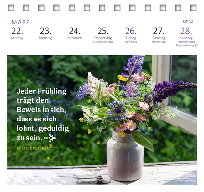 Gezeigt wird eine Innen- oder Zusatzansicht von „Postkartenkalender Gartenglück 2027“. Die Darstellung zeigt eine üppige Blumenkomposition in einem weißen, leicht gebogenen Blumentopf, die vor einem geöffneten Fenster platziert ist. Die Farben sind lebhaft und vielfältig, einschließlich Lila, Blau, Gelb und Grün. In der linken Bildhälfte befindet sich ein Zitat von Gustave Flaubert in eleganter, gut lesbarer Schrift, das in Weiß auf einem tiefgrünen Hintergrund erscheint. Der...